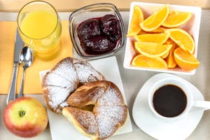 Fresh continental breakfast with croissant, coffee, orange slices, juice, jam, and apple, served on a plate.