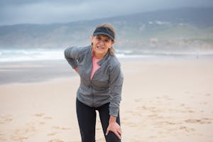 Senior woman resting during her fitness routine on a beach in Portugal, enjoying the outdoor scenery.